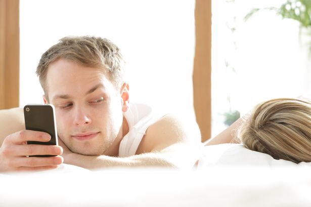 Man-with-phone-in-bed-looking-at-woman-asleep